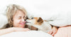 A dog licks a young woman's face while she lays in her bed.